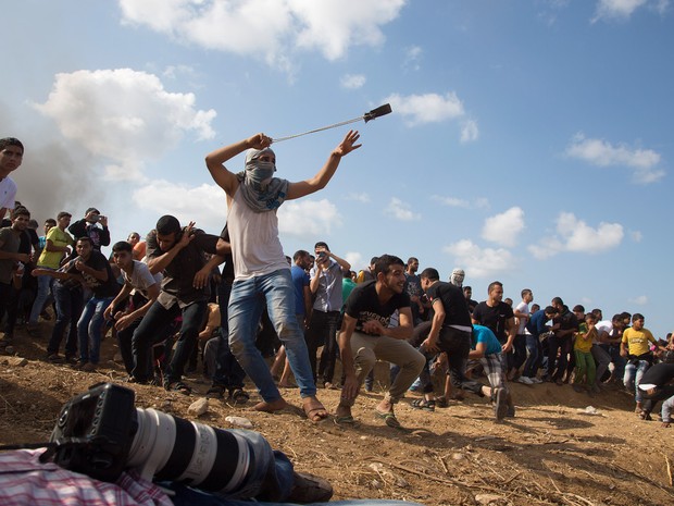 Um manifestante palestino atira pedras em soldados israelenses durante confrontos na fronteira israelense  da Cidade de Gaza. Seis palestinos morreram  (Foto: Adel Hana/AP)