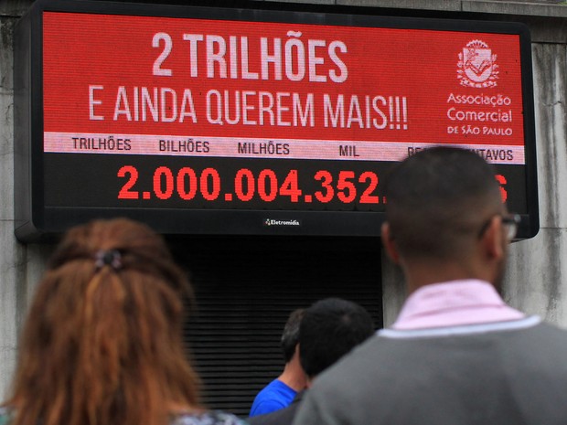 Pessoas observam painel eletrônico da Associação Comercial de São Paulo, instalado no centro da cidade, que indica a arrecadação de 2 trilhões de reais de impostos em 2015 (Foto: Werther Santana/Estadão Conteúdo)