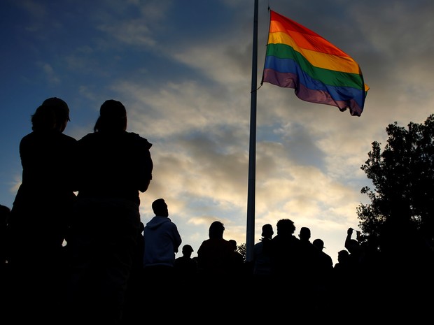 Pessoas se reúnem ao redor de uma bandeira do orgulho LGBT hasteada a meio mastro para uma vigília à luz de velas em memória das vítimas do ataque à boate Pulse em Orlando, na madrugada de domingo (12), em San Diego, nos EUA (Foto: Mike Blake/Reuters)