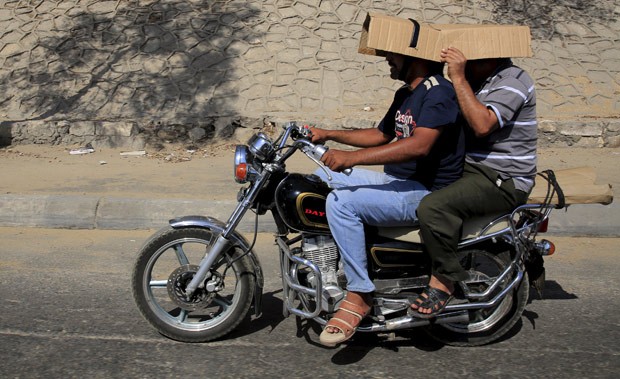 Sem capacetes, uma dupla usou um papelo para se proteger no sol enquanto andava de moto na cidade do Cairo, no Egito, na segunda-feira (17) (Foto: Amr Abdallah Dalsh/Reuters)