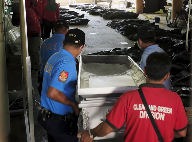 Membros da Polícia Nacional das Filipinas e outras pessoas carregam um caixão vazio em direção a corpos das vítimas do incêndio em uma fábrica em Manila (Foto: Romeo Ranoco/Reuters)