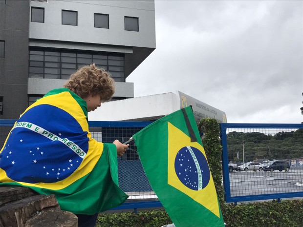 Criança coberta pela bandeira do Brasil aguarda a chegada de Sérgio Cabral à Polícia Federal de Curitiba (Foto: Rafael Nascimento/ RPC Curitiba)