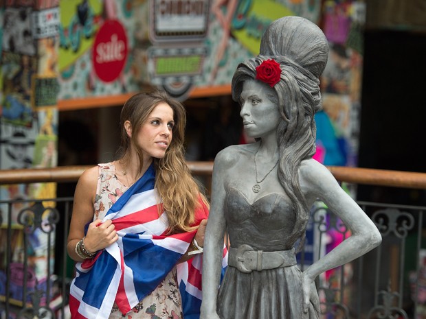 Uma fã posa ao lado da estátua em homenagem à cantora Amy Winehouse, que foi inaugurada neste domingo (14) no Camden's Stables Market, bairro de Londres (Foto: AP Photo/Tim Ireland)