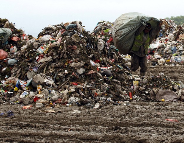 Sérvio carrega saco com centenas de garrafas plásticas em um lixão a cerca de 15 km da capital do país, Belgrado. O lixo vem causando problemas ambientais e bloqueando rios e riachos no país, segundo agências internacionais (Foto: Darko Vojinovic/AP)