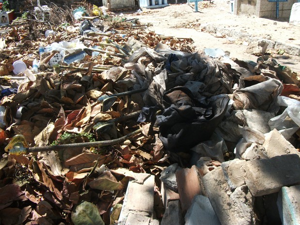 Mortalhas, restos de ossadas e caixão abandonados junto ao lixo que fica dentro do cemitério (Foto: Waldson Costa/G1)
