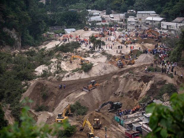 Equipes de resgate fazem busca por sobreviventes após um deslizamento de terra em Cambray, um bairro no subúrbio de Santa Catarina Pinula, a leste da Cidade da Guatemala. Uma colina desabou após fortes chuvas, enterrando várias casas  (Foto:  Moises Castillo/AP)