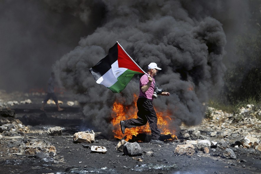 Um homem carrega uma bandeira Palestina durante choques com o exército de Israel. Os palestinos protestam contra a construção de um assentamento de Israel na cidade de Qadomem, na Cisjordânia