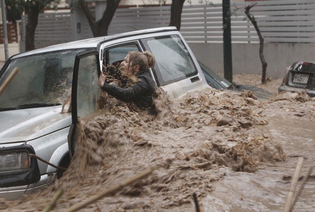 Mulher se esforça para deixar seu carro, com a força da água dificultando a saída no subúrbio ao norte de Atenas (Foto: John Kolesidis/Reuters)