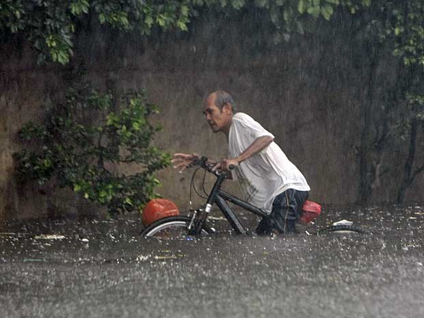 Sem conseguir pedalar sua bicicleta, homem enfrenta rua inundada no subúrbio de Quezon para recuperar uma bola. (Foto: Bullit Marquez / AP Photo)