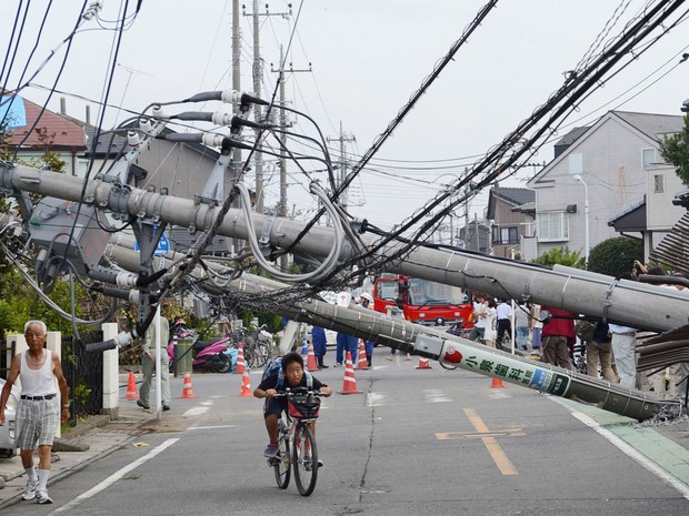 Jovem passa de bicicleta por baixo de um poste caído durante a passagem de um tornado em Koshigaya, no Japão. Dezenas de pessoas ficaram feridas em decorrência do fenômeno, segundo a mídia local. (Foto: AP/Kyodo)