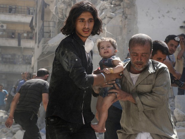 Voluntário e membro da defesa civil da Síria carregam bebê encontrada sob escombros de um edifício destruído depois de um ataque aéreo no norte de Aleppo (Foto:  Thaer Mohammed/AFP)