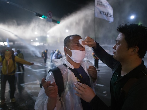 Um manifestante sul-coreano ajuda colega atingido por canhão de água durante protesto em Seul, na sexta (1º) (Foto: AFP Photo/Ed Jones)