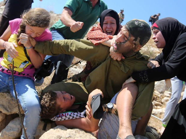 Menina palestina morde a mão de um soldado israelense, que é atacado por mulheres após imobilizar um menino durante confronto na vila de Nabi Saleh, perto de Ramallah, na Cisjordânia. Manifestantes protestavam contra o confisco de terras palestinas (Foto: Abbas Momani/AFP)