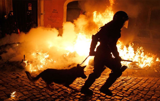 Policial passa por foto ateado por manifestantes durante protesto em Lisboa, Portugal, nesta quarta-feira (14) (Foto: AFP)