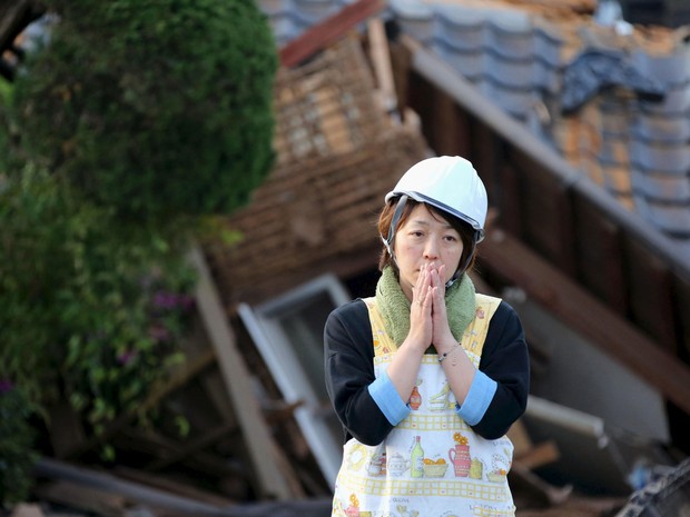 Mulher olhadesolada para casa destruída após terremoto no Japão (Foto: Reuters/Kyodo)