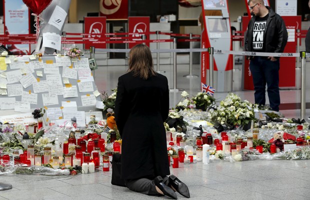 Mulher ajoelha em frente a velas e flores deixadas no aeroporto de Duesseldorf, na quarta-feira, em homenagem à tragédia aérea (Foto: Wolfgang Rattay/Reuters)