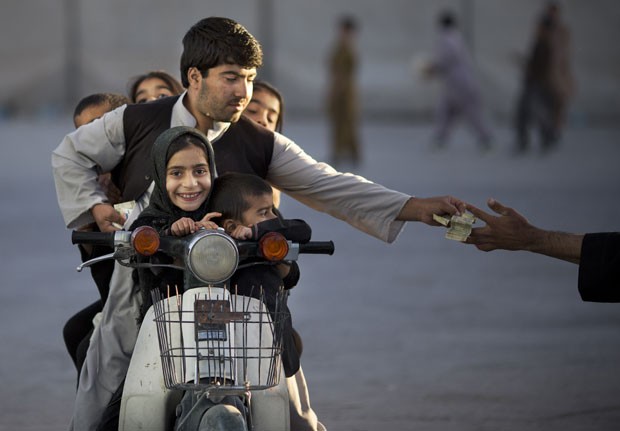 Um motociclista foi flagrado levando cinco crianças em uma motoneta enquanto pagava para entrar em um parque em Kandahar, no Afeganistão, nesta sexta-feira (1º) (Foto: Anja Niedringhaus/AP)