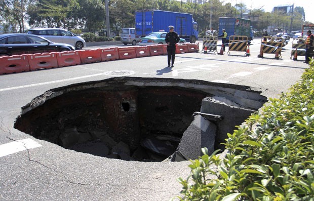 Policial é visto ao lado de buraco gigante aberto em asfalto na China. Um carro chegou a ficar preso, mas foi retirado e ninguém ficou ferido (Foto: Reuters)