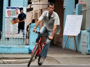 Ciclista circula próximo a cartazes que promovem um restaurante privado em Havana, Cuba (Foto: Alejandro Ernesto/EFE)