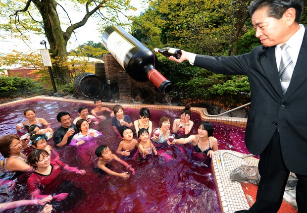 Sommelier Shunji Kanaya derruba um pouco mais do vinho na piscina, enquanto os visitantes se divertem e brindam ao vinho. (Foto: Toshifumi Kitamura/AFP)