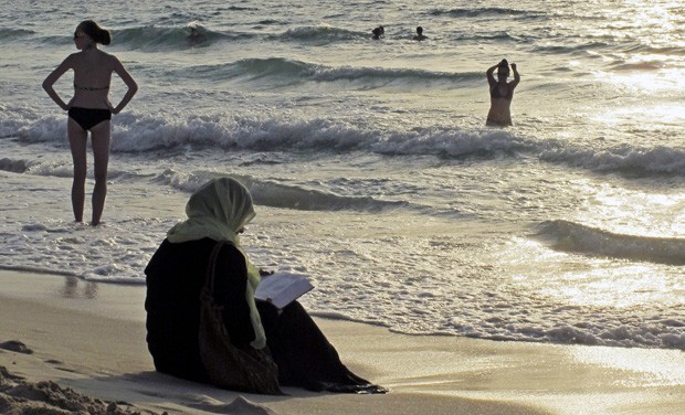 Mulher lê sentada na areia em Dubai, em foto tirada em setembro do 2012. Emirados Árabes Unidos aprovou recentemente a proibição de 'trajes de banho reveladores' em praias públicas da confederação (Foto: Hassan Ammar/AP)