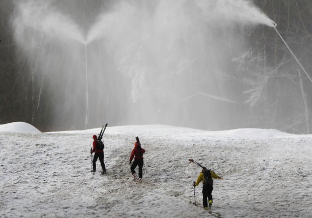 Esquiadores debaixo de neve fabricada pelos canhões (Foto: Toby Talbot/AP)