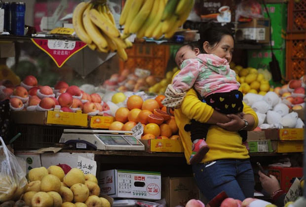 Mulher com bebê compra frutas em feira em Xangai nesta sexta-feira (9) (Foto: AFP)
