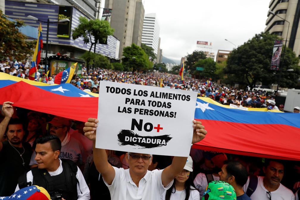 No Dia do Trabalhador, manifestantes seguram bandeira da Venezuela e cartaz onde se lê: 'Todos os alimentos para todas as pessoas! Sem mais ditadura'; protesto contra o presidente venezuelano, Nicolás Maduro, aconteceu em Caracas nesta segunda-feira, dia 1º de maio de 2017 (Foto: Carlos Garcia Rawlins/Reuters)