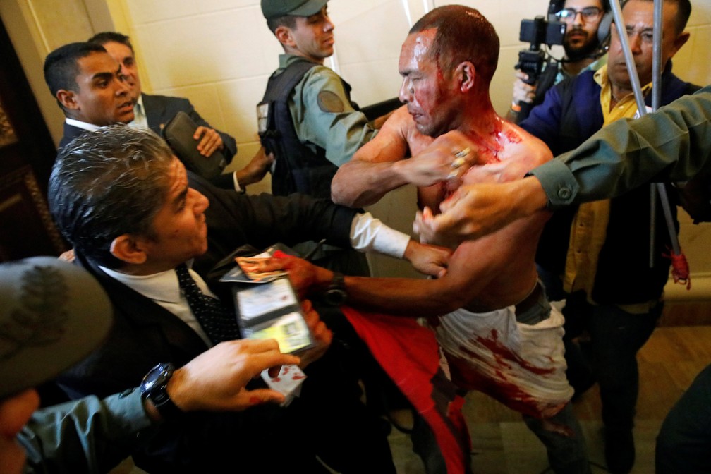 Homem ferido coberto de sangue tenta deixar A Assembleia Nacional da Venezuela depois que ele e um grupo de apoiadores do governo de Nicolas Maduro invadiram a sede do Legislativo, controlada pela oposição, em protesto durante uma sessão parlamentar (Foto: Carlos Garcia Rawlins/Reuters)