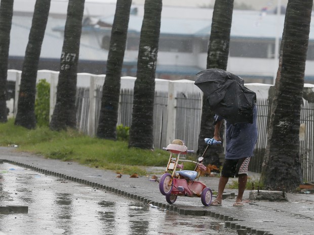 Homem segura triciclo infantil enquanto enfrenta ventos fortes durante a passagem de tufão nas Filipinas (Foto: AP Photo/Bullit Marquez)