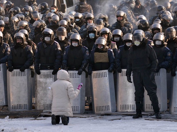 Ajoelhada, mulher fala com policiais compondo uma barreira para conter os protestos em Kiev, na Ucrânia. O acampamento dos manifestantes foi movido nesta sexta-feira (24) na direção do palácio do presidente Viktor Yanukovych. (Foto: Sergei Supinsky/AFP)