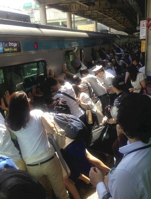 Passageiros e funcionários de trem empurram vagão para ajudar no resgate de uma mulher que caiu no vão entre a plataforma na China (Foto: orihiro Shigeta, Yomiuri Shimbun/ AP)