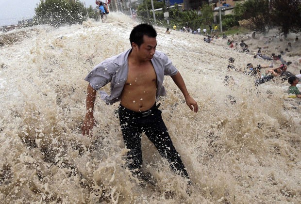 Homem tenta se manter em pé enquanto outras, ao fundo, são arrastadas em Qiantang (Foto: Reuters/China Daily)