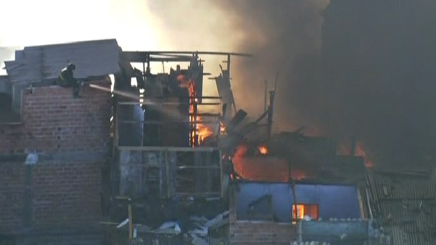 Bombeiros tentam controlar fogo em barracos (Foto: Reprodução/TV Globo)