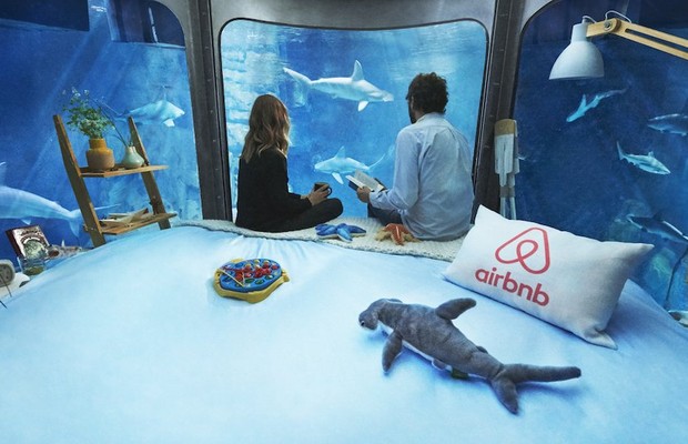 Casal sentado do tanque de tubarões oferecido pelo Airbnb (Foto: airbnb.com)