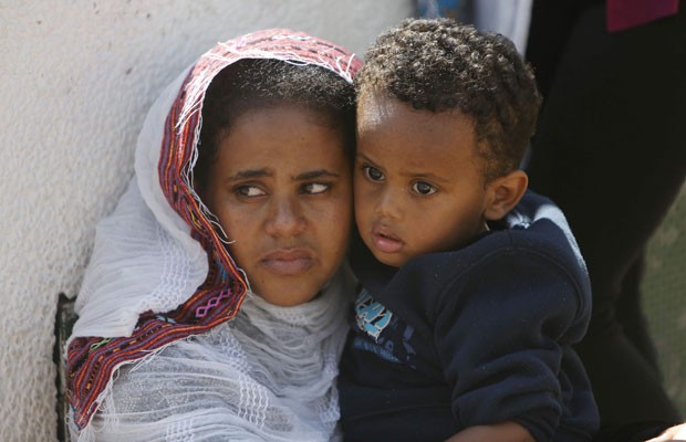 Em Tel Aviv, neste sábado (12), mulher africana e seu filho assistem a memorial pelas mortes de centenas de imigrantes no naufrágio em Lampedus, na semana passada. A Itália pede mais apoio da União Europeia e uma revisão das regras de imigração do bloco depois do naufrágio na costa da Sicília. (Foto: Nir Elias/Reuters)