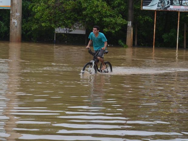 Homem se arrisca em bicicleta para atravessar rua alagada (Foto: Tássio Andrade/G1)