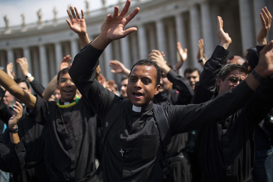 Padres cantam e dançam na Praça São Pedro, no Vaticano, enquanto peregrinos e fiéis se reúnem para esperar a cerimônia de canonização dos papas