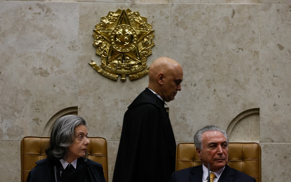 O novo ministro do STF Alexandre de Moraes (centro), a caminho da assinatura do termo de posse; sentados, a presidente da Corte, Cármen Lúcia, e o presidente da República, Michel Temer (Foto: Beto Barata/PR)