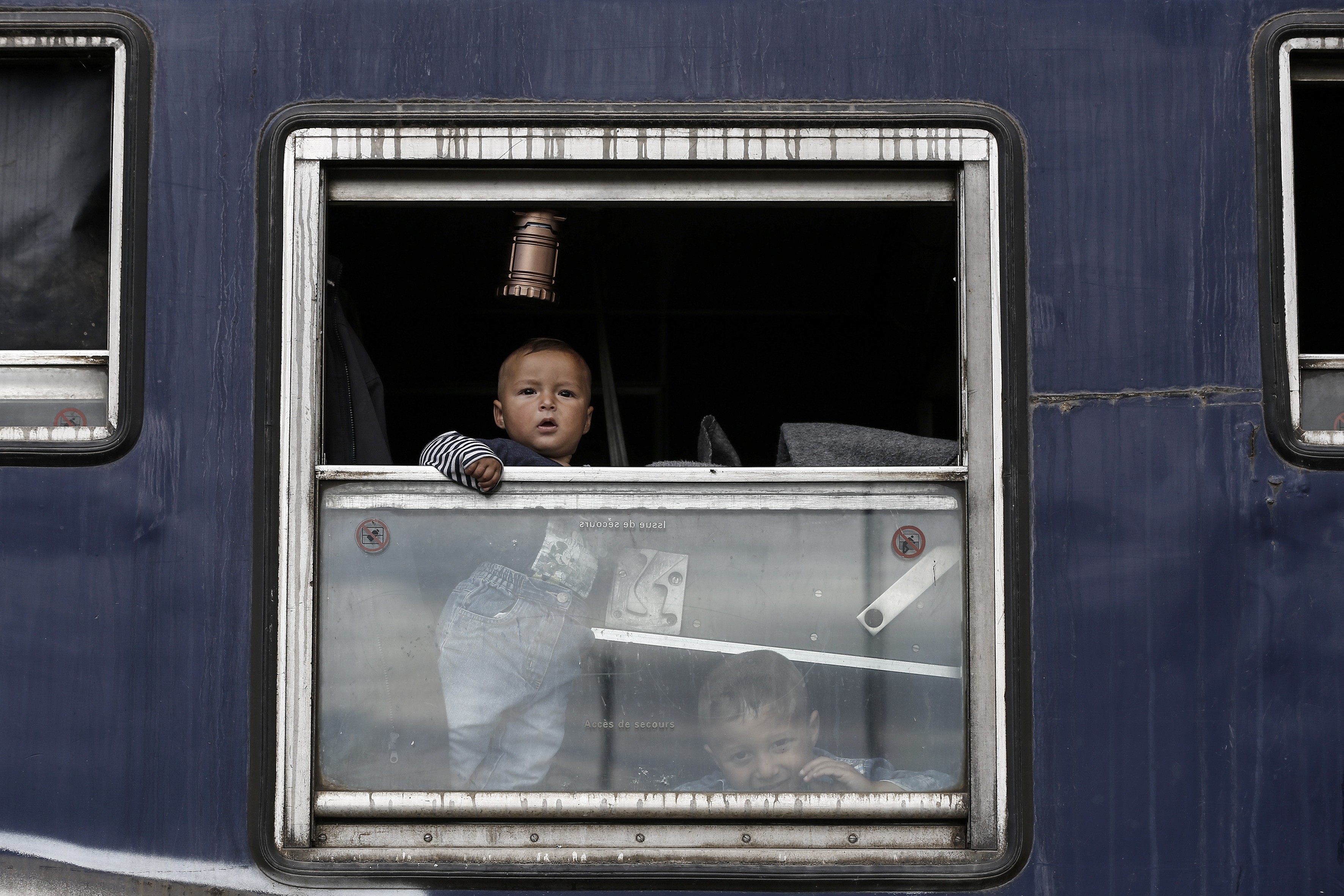 Crianças olham por janela durante opeação para esvaziar o campo de Idomeni (Foto: Yannis Koledis/AFP)