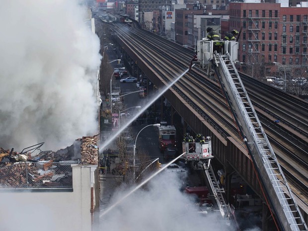 Bombeiros trabalham controlando o fogo ao lado dos trilhos do metrô sobre a Park Avenue, em Nova York (Foto: John Minchillo/AP)