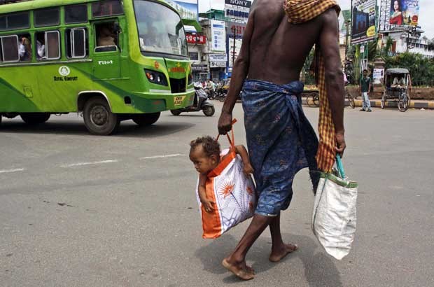 Homem indiano carrega seu filho em uma sacola pelas ruas em Bhubaneswar, na Índia (Foto: Biswaranjan Rout/ AP)