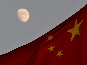 Bandeira chinesa é vista em frente à lua na Praça Tiananmen, em Pequim, nesta sexta-feira (13); veículo lunar chinês deve pousar na Lua neste sábado. (Foto: AFP Photo/Mark Ralston)