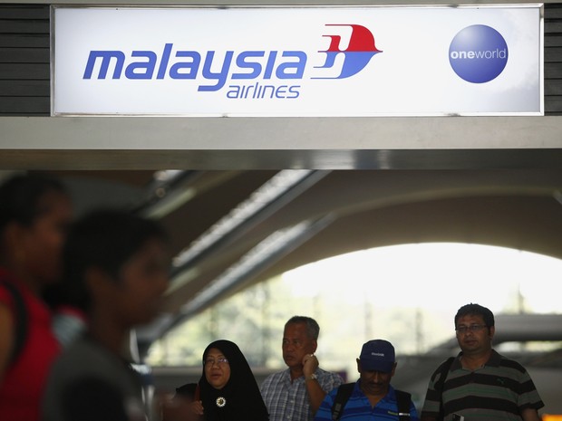 Pessoas passam por anúncio da Malaysia Airlines no Aeroporto Internacional de Kuala Lumpur, em Sepang, Malásia, neste sábado (8). O voo que ia de Kuala Lumpur a Pequim, na China, está desaparecido. Aeronave levava 239 pessoas a bordo. (Foto: Samsul Said/Reuters)