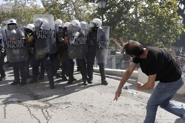 Manifestante joga pedra em policiais durante confronto em Atenas, na Grécia, nesta quinta-feira (18) (Foto: AFP)
