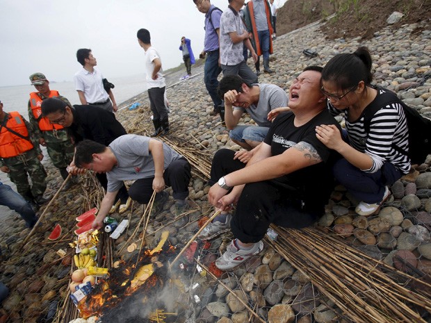 Familiares das vítimas do naufrágio do navio "Dongfangzhixing" ("Estrela do Oriente") choram enquanto queimam oferendas na província de Hubei, na China, neste domingo (7) (Foto: REUTERS/Chen Zhuo/Yangzi River Daily)