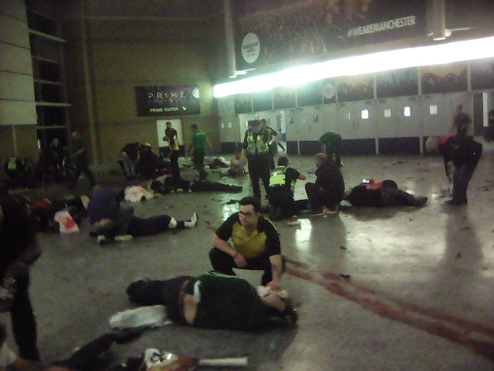 Policiais e outras pessoas tentam socorrer feridos após explosão na Manchester Arena durante show da cantora Ariana Grande na noite de segunda-feira (22) (Foto: PA via AP)