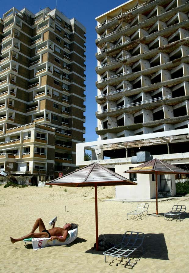  Em foto de 2003, um turista lê um livro em frente a um hotel destruído em Varosha (Foto:  AP Photo/Petros Karadjias)