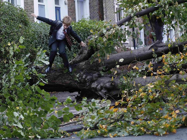 No caminho para a escola, menino pula árvore derrubada pela tempesdade no norte de Londres, na Inglaterra. Temporal e fortes ventos causaram centenas de alertas por inundações no país. (Foto: Olivia Harris/Reuters)
