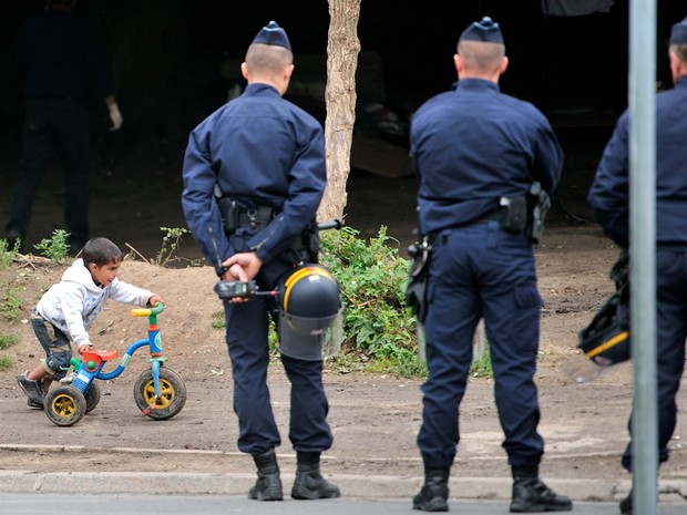 Uma criança caminha perto de policiais enquanto aguardam a saída de ciganos de um acampamento em Villeneuve d'Ascq, norte da França. (Foto: PHILIPPE HUGUEN/AFP)